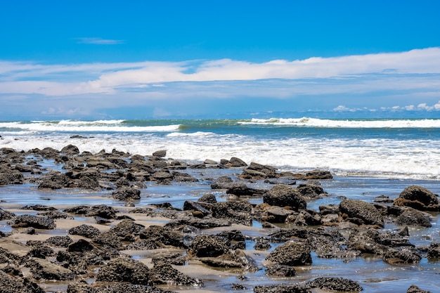 Praia de pedras rochosas com ondas sob o céu azul brilhante