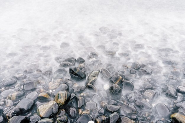 Praia de seixos do mar com pedras multicoloridas, ondas transparentes com nevoeiro