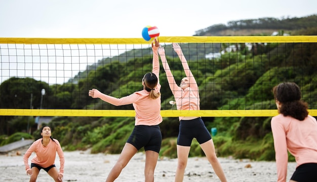 Praia de vôlei e competição com mulheres esportivas jogando um jogo ao ar livre para treinamento no verão Esporte de equipe e bola com amigas na areia da costa para jogar uma partida competitiva