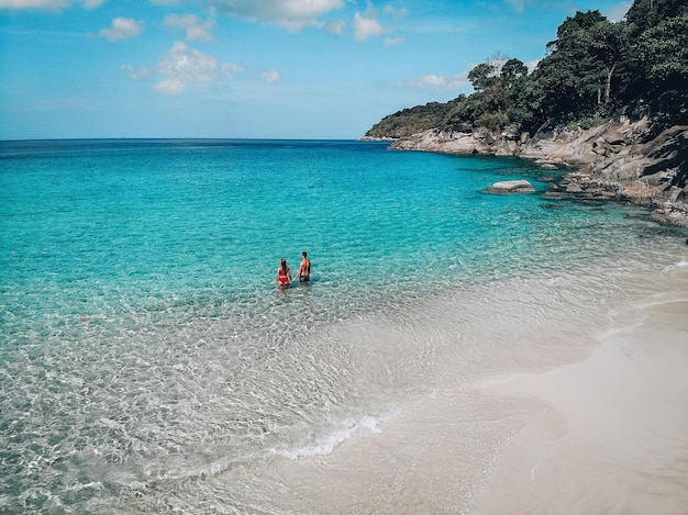 Praia drone vista Ilha tropical de Phuket, praia branca com ondas, casal deitou-se na praia, homem e mulher. Foto aérea. Viagem para um destino quente.