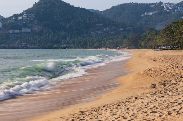 Praia ensolarada tropical vazia com ondas batendo na costa e montanhas no fundo Samui Tailândia