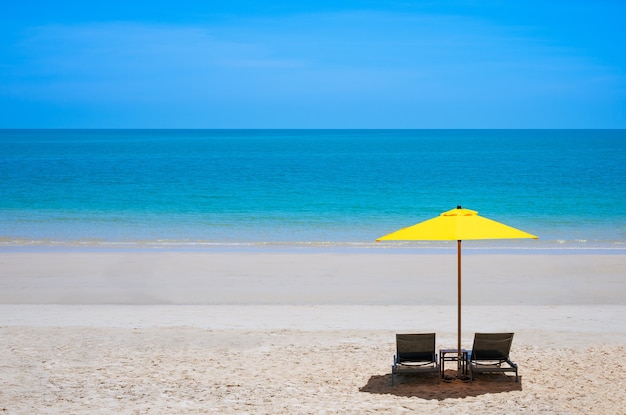 Praia marítima com duas espreguiçadeiras sob um guarda-sol amarelo no verão