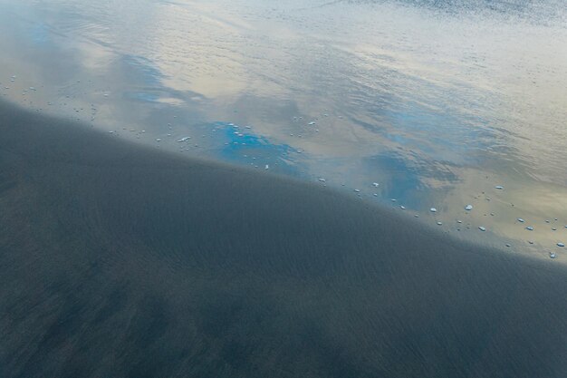 Foto praia oceânica com areia vulcânica preta o céu é refletido na onda revertida da ressaca