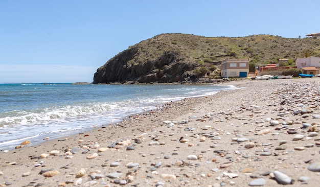 Praia onde existe um grande rochedo e a seus pés casas de marinheiros com seus barcos de pesca e equipamentos.