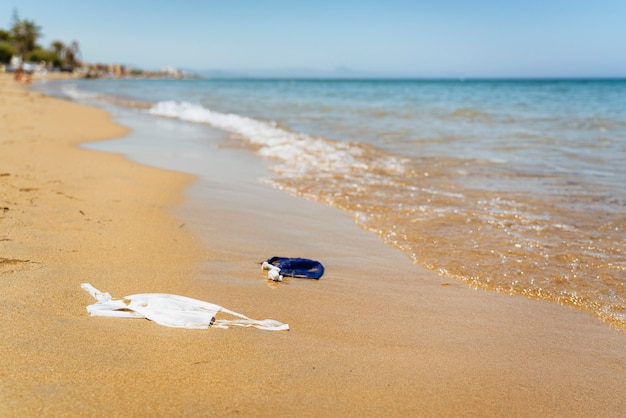 Praia poluída com máscaras de cobertura. Problema de contaminação ambiental