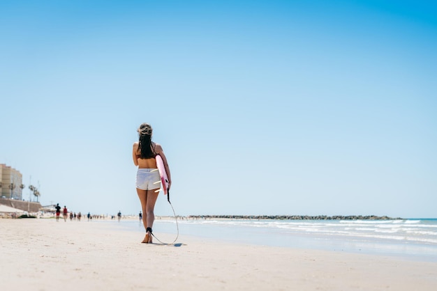 Praia semi-deserta e uma garota indo para longe com uma prancha de surf