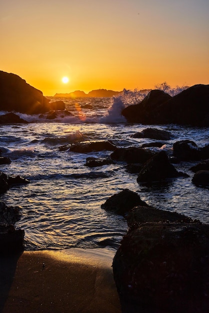 Praias da Califórnia com ondas do mar batendo sobre rochas durante o pôr do sol