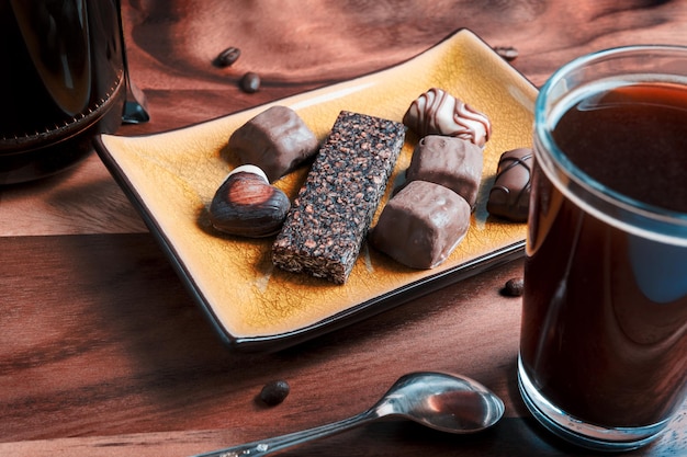 Pralinen und Müsliriegel in einem Teller mit einer Tasse Kaffee und einer Kaffeemaschine auf einem Holzbrett