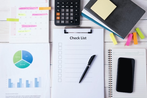 Foto prancheta com papel em branco de lista de verificação com caneta e telefone inteligente no notebook com calculadora e documento, calendário tem plano de memorando. vista do topo.