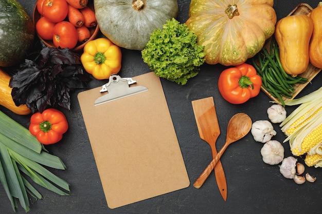 Prancheta e utensílios de cozinha cercados por vegetais frescos em preto