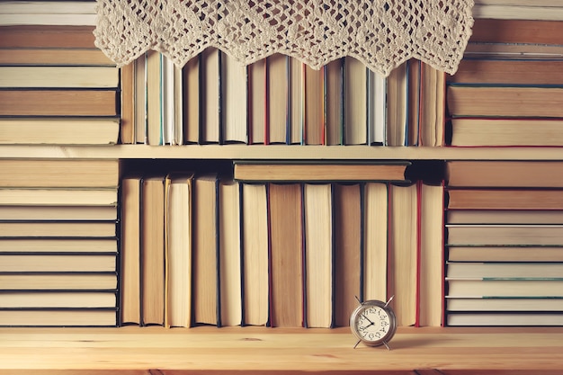 Foto prateleira cheia de livros. um monte de livros, um despertador e um guardanapo de renda em uma prateleira de madeira.