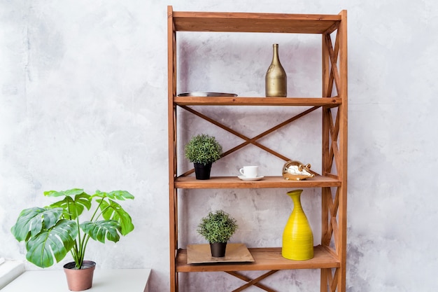 Prateleira de madeira com elementos decorativos e planta em vaso apoiada em parede cinza. foto horizontal