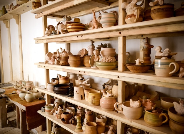 Prateleiras de madeira em uma olaria em que há cerâmicas, muitas cerâmicas diferentes nas prateleiras de uma olaria. Luz baixa