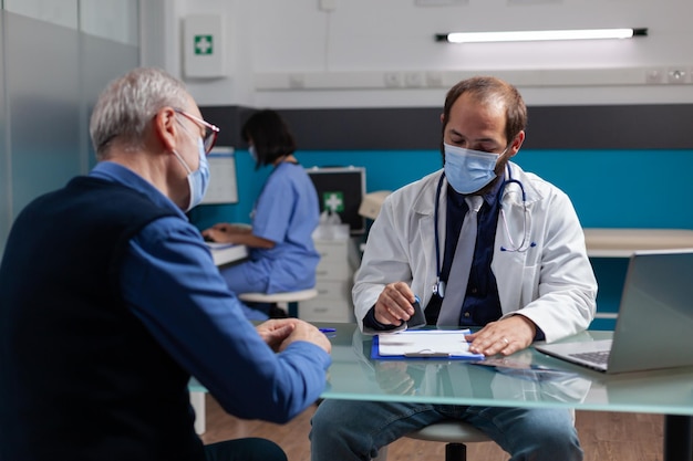 Praticante colocando selo médico em papel de prescrição para dar remédios de saúde ao homem sênior no cargo. Médico usando carimbo no relatório de visita de check-up durante a pandemia de coronavírus.