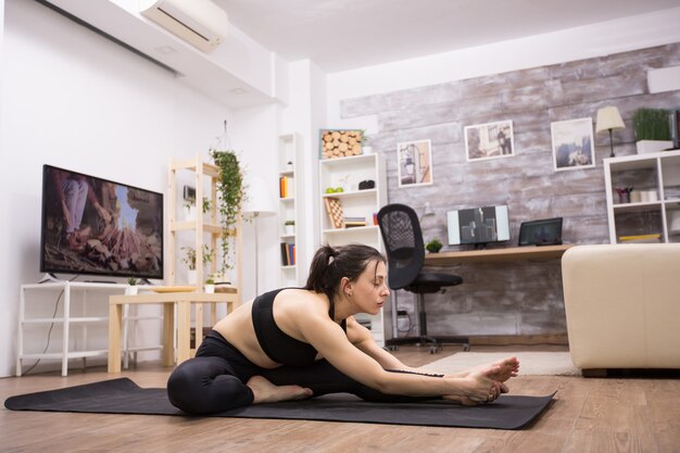 Praticante de ioga feminina fazendo seus exercícios em casa, vestindo roupas esportivas pretas.