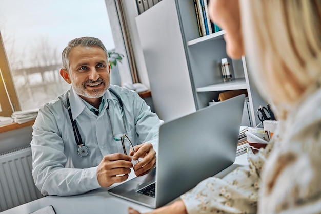 Praticante emocional positivo sentado à mesa em frente a um paciente idoso feliz e sorrindo para ela