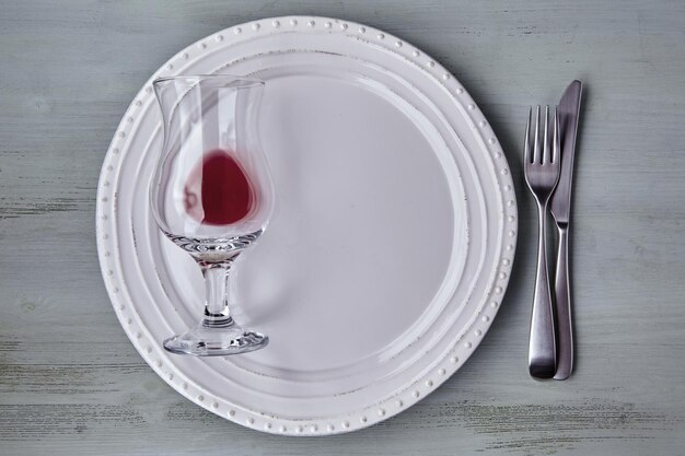 Prato branco com talheres com um copo de vinho em uma mesa de madeira azul vista superior plana