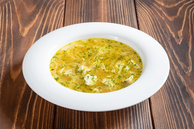 Foto prato branco de sopa de galinha quente com macarrão na mesa de madeira