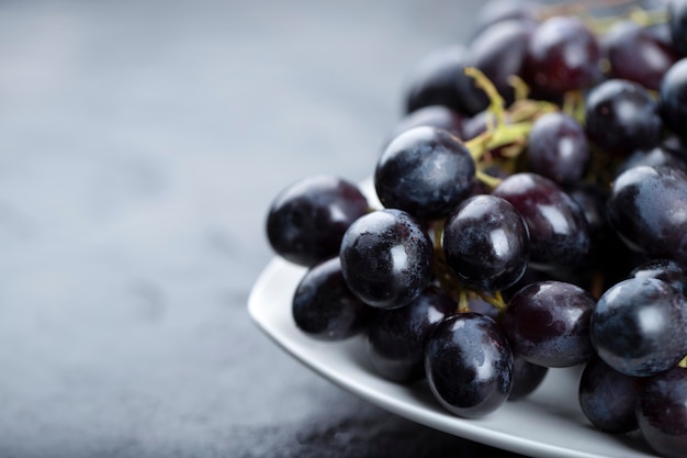 Prato branco de uvas frescas pretas sobre fundo preto.