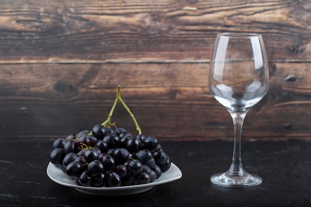 Prato branco de uvas pretas e copo de vinho branco na superfície preta