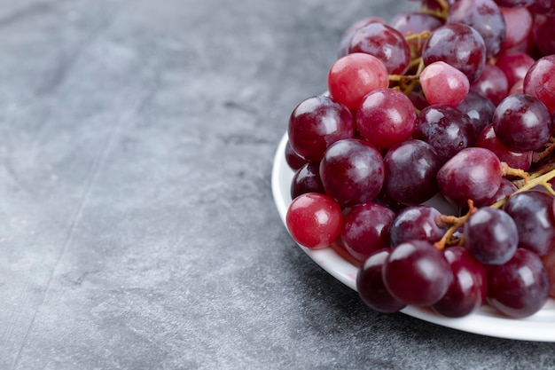 Prato branco de uvas vermelhas frescas em fundo de pedra.