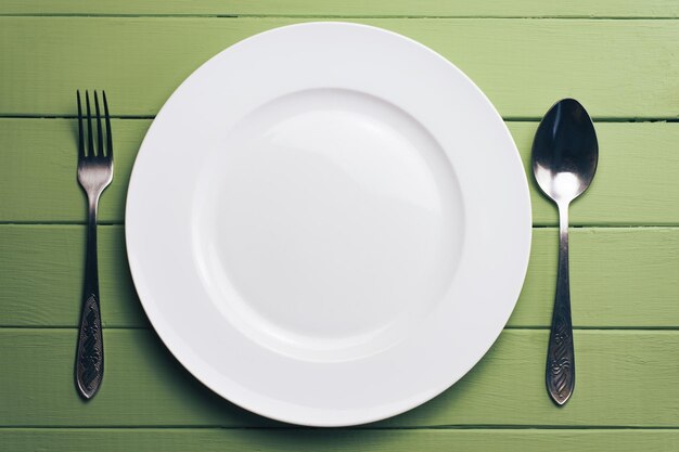 Prato branco e um garfo com uma colher em um fundo de mesa de madeira verde