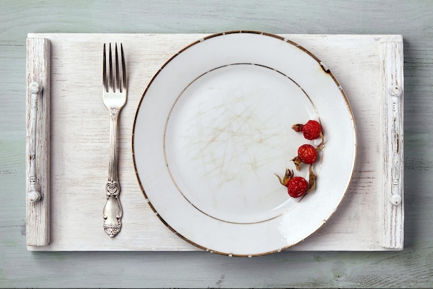 Prato branco vintage guarnecido com rosa mosqueta com um garfo em uma bandeja de madeira em uma mesa azul Maquete de menu de vista superior
