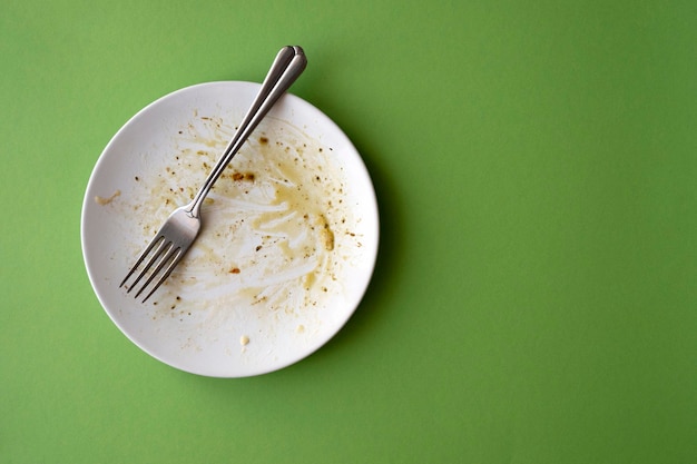 Prato cerâmico branco com restos de comida molho de azeite e garfo sobre fundo verde