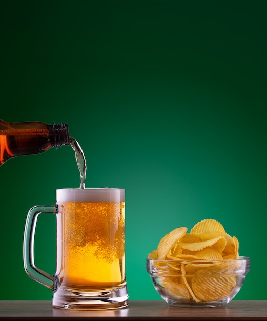 Prato com batatas fritas e cerveja light despejando caneca sobre fundo verde