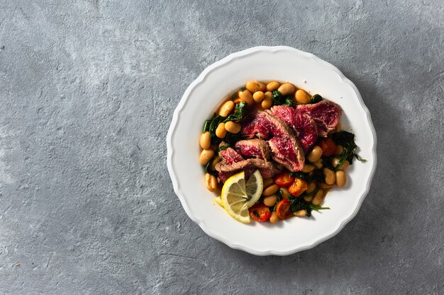 Prato com carne, feijão branco, espinafre e tomate vista superior