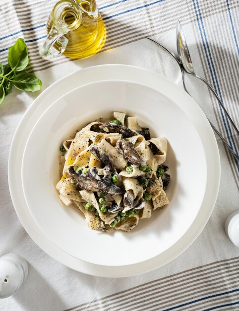 Prato com cogumelos de macarrão tagliatelle e ervilhas verdes em cima da mesa