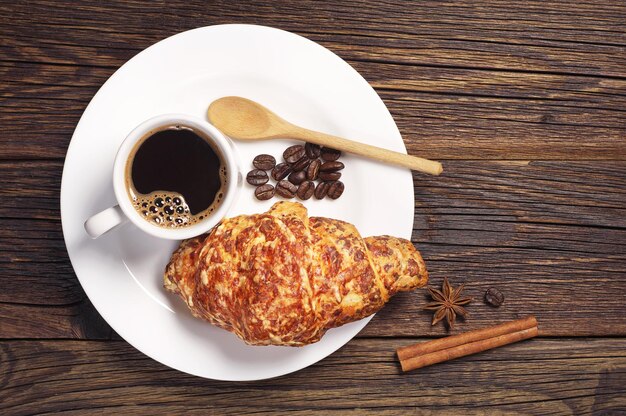 Prato com croissant e xícara de café na mesa de madeira escura, vista superior