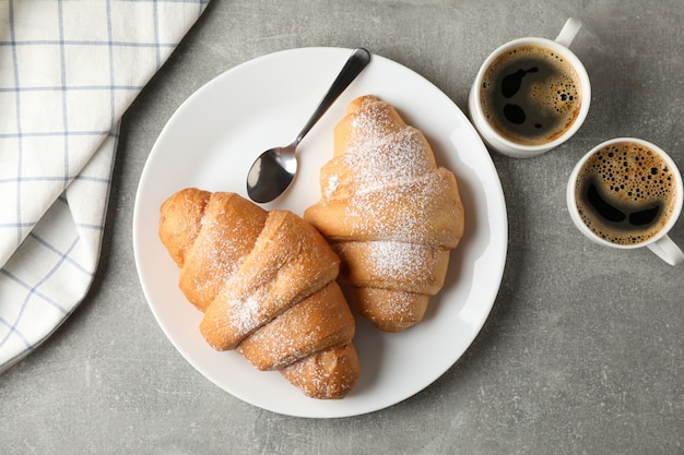 Prato com croissants, xícaras de café e toalha no fundo cinza, vista superior