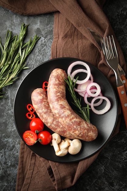 Prato com linguiça crua e ingredientes na mesa de fumaça preta