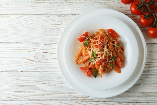 Prato com macarrão com molho de tomate e tomate na mesa de madeira branca