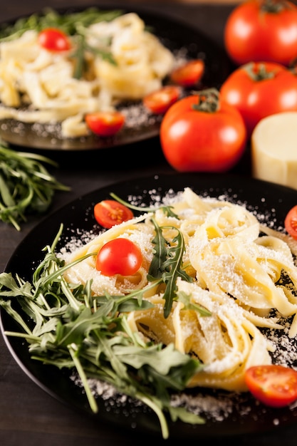 Prato com macarrão tagliatelle, tomate cereja e folhagem na mesa de madeira