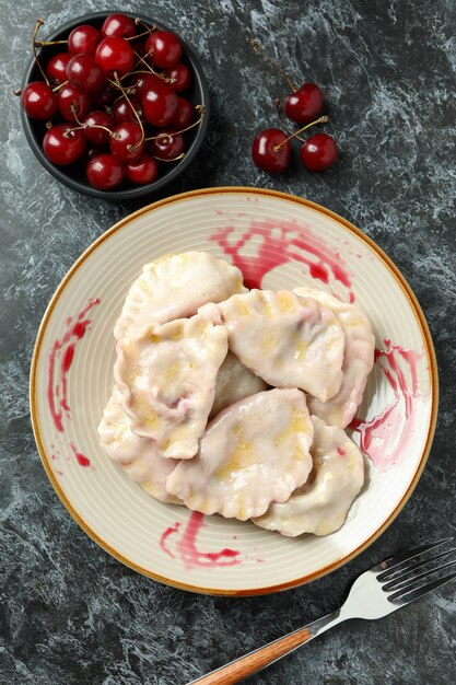 Prato com pierogi com cereja em fundo preto esfumaçado