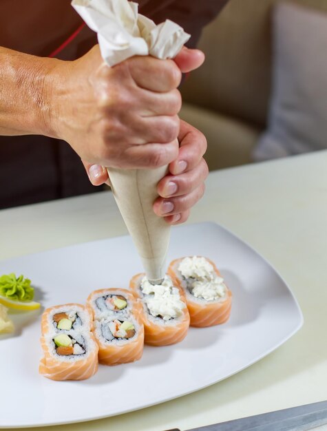 Prato com rolos de sushi. Homem segura um saco de confeitar. O chef adiciona queijo cremoso fresco. Decoração de rolos de uramaki.