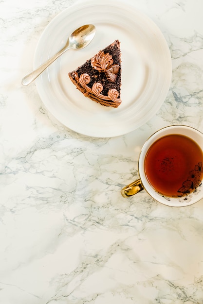 Prato com uma fatia de bolo de chocolate caseiro e uma xícara de chá de ouro amarelo sobre fundo de mármore. Copie o espaço. Vista superior. Conceito de café da manhã do feriado de ano novo de Natal