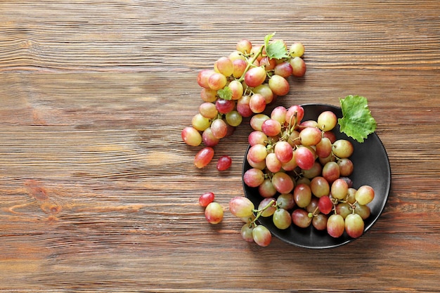 Prato com uvas frescas maduras em fundo de madeira