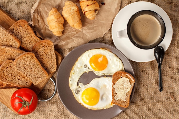 Prato com xícara de ovos fritos de croissants de café preto e pão