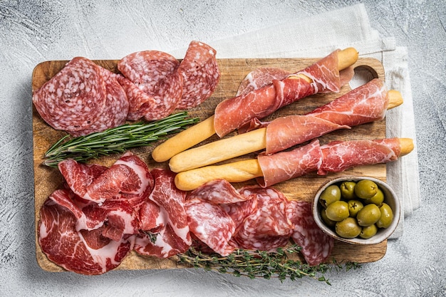 Prato de antepasto de carnes frias com palitos de pão grissini Prosciutto crudo Salame e linguiça Coppa Fundo branco Vista superior