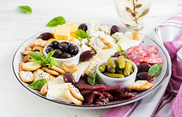 Prato de antipasto com basturma, salame, queijo azul, nozes, picles e azeitonas sobre um fundo de madeira branca