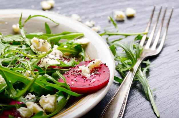 Prato de argila com rúcula de beterraba e salada de queijo feta na bandeja de ardósia vista aproximada Garfo à parte