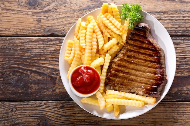 Prato de bife grelhado com batatas fritas na mesa de madeira, vista superior