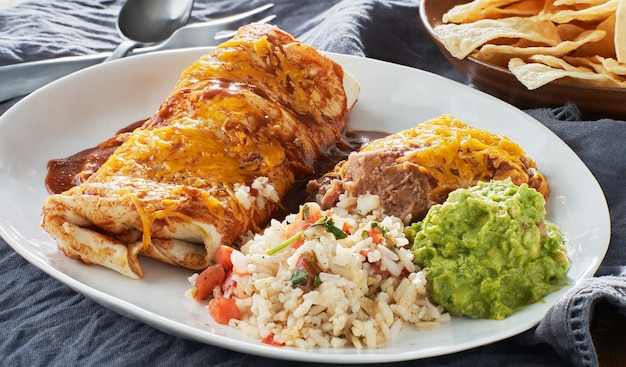 Foto prato de burrito mexicano com molho de enchilada vermelha, feijão frito, arroz e guacamole