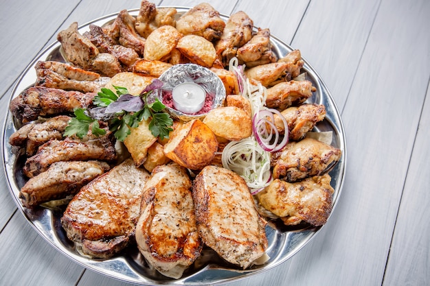 Prato de carne com deliciosos pedaços de carne, batata, cebola e vela na mesa de madeira branca