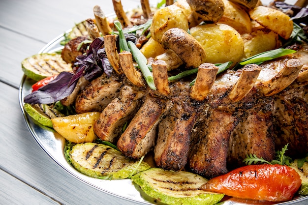 Prato de carne com deliciosos pedaços de carne, salada, costelas, legumes grelhados e batatas na mesa de madeira branca