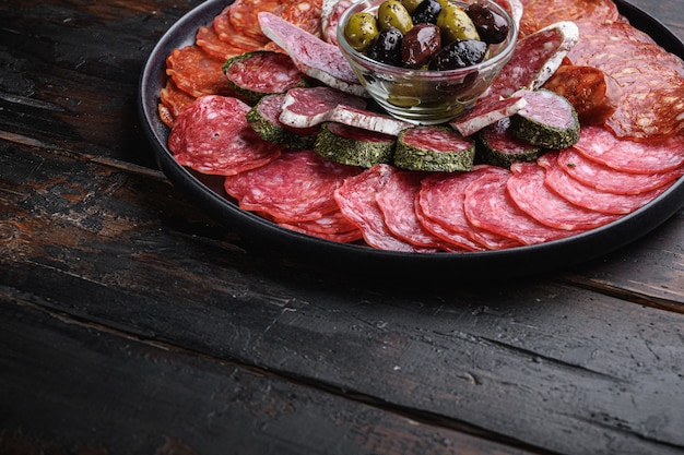 Prato de carne curada de tapas espanholas tradicionais. Chouriço, salchichon, longaniza e fuet no fundo escuro de madeira com espaço para texto.