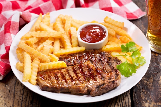 Prato de carne grelhada com batatas fritas na mesa de madeira